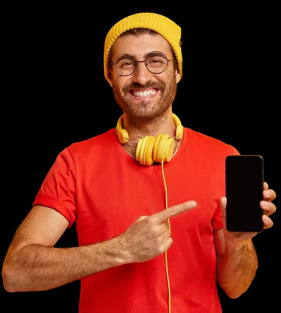 Joven portando unos audífonos sobre su cuello y señalando un celular